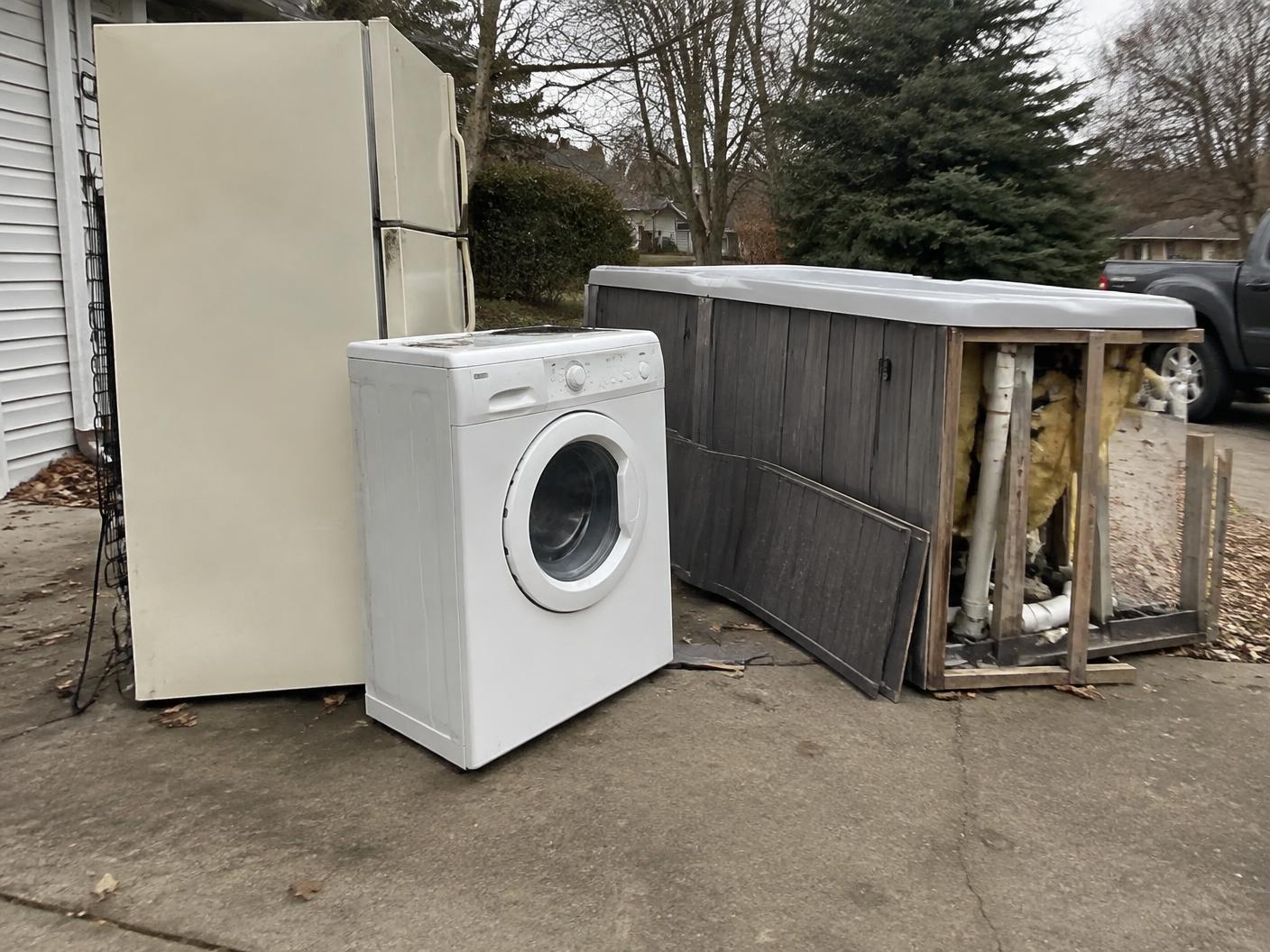Old refrigerator, washing machine and dismantled hot tub on a driveway