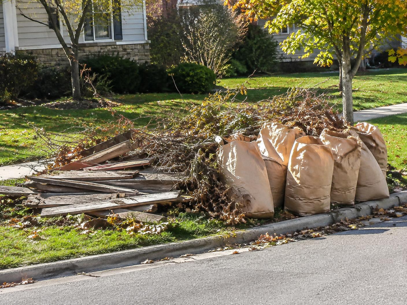 Curbside pile of branches, bagged leaves and old fence boards